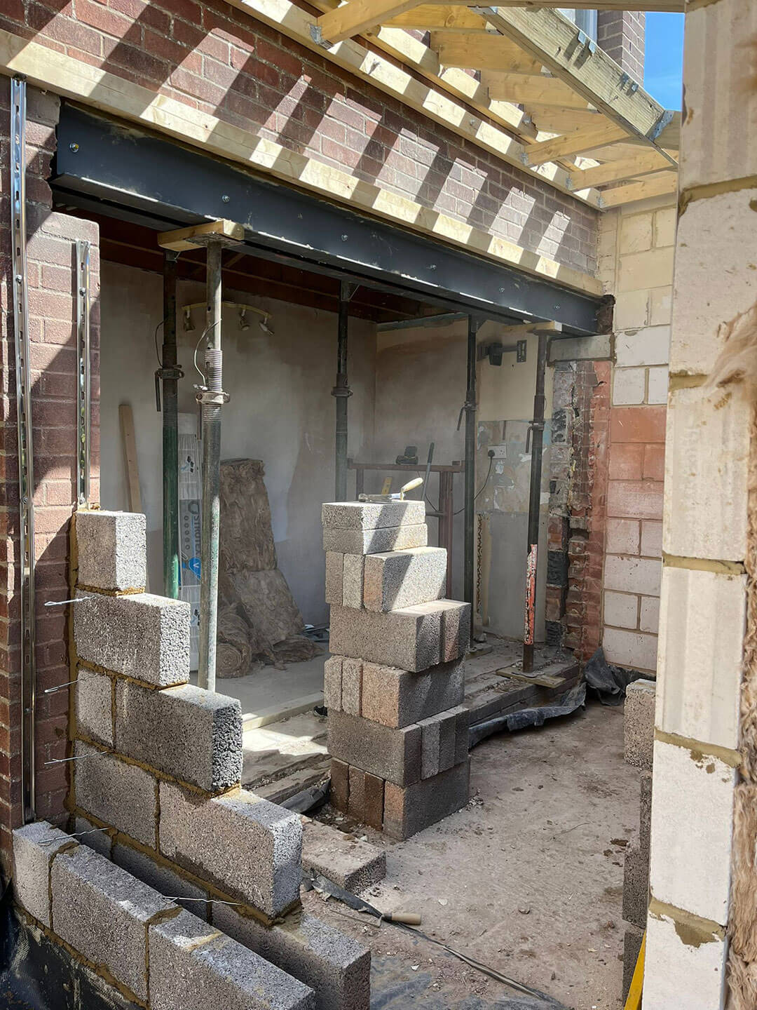 A steel beam in place over a newly formed opening, acrow props still carrying the load and blockwork going up beneath it