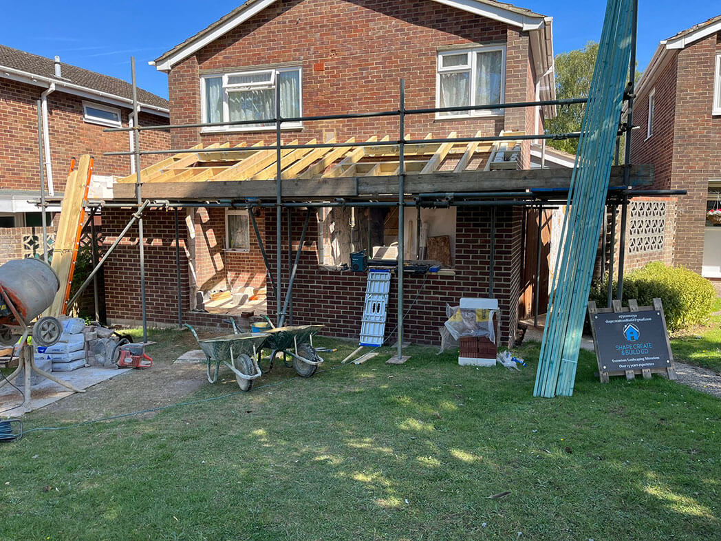 A house part-way through a front extension, the new roof structure timbered out, scaffold up and the site in use