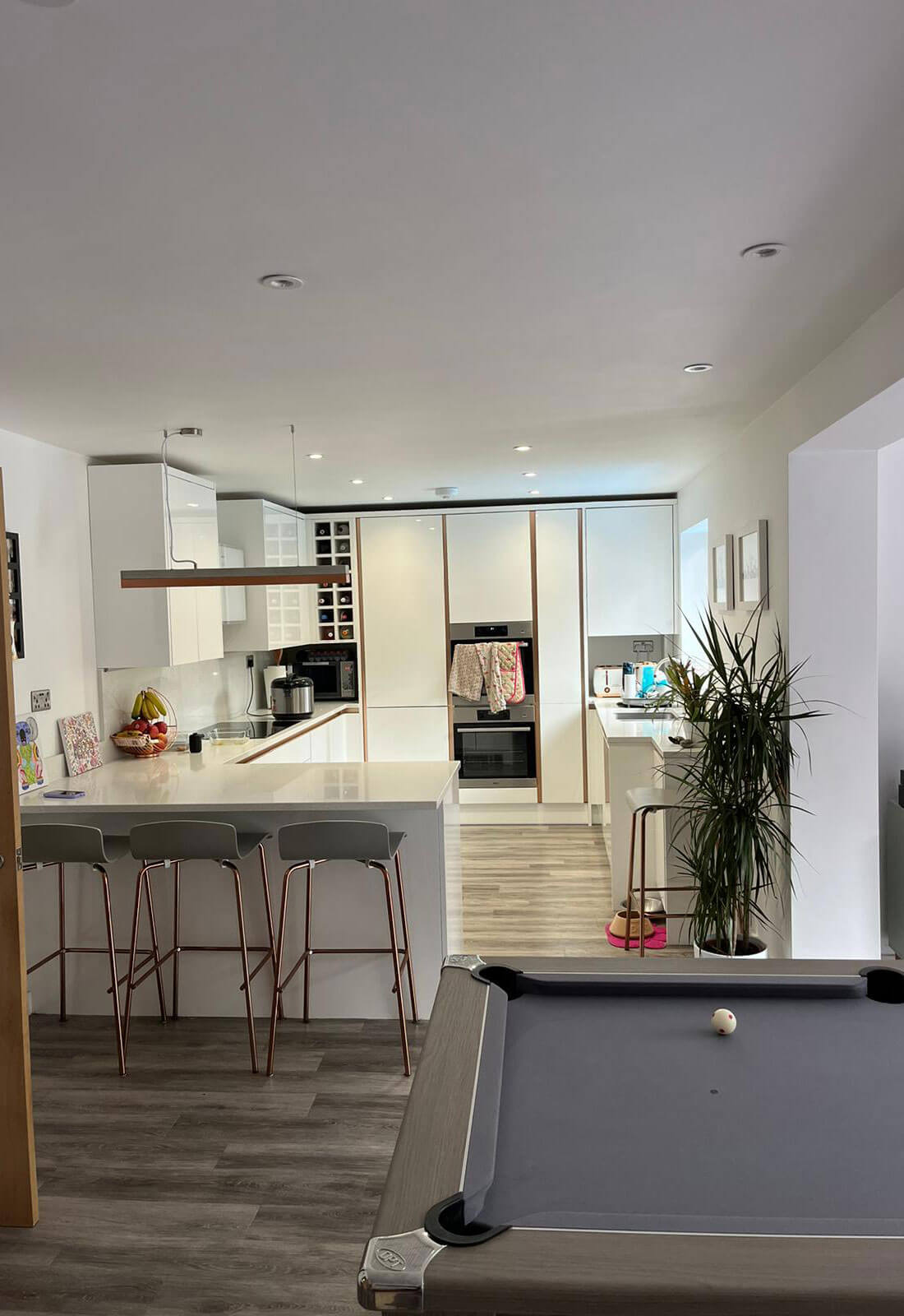 A finished handleless kitchen with a breakfast bar, built-in ovens and new flooring running through to the room beyond