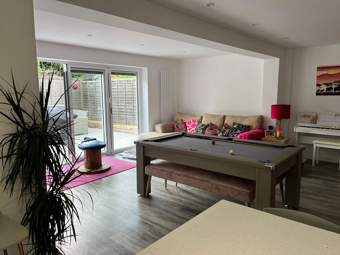 A finished open-plan living room with new flooring, a downstand where the wall used to be, and sliding doors onto the garden