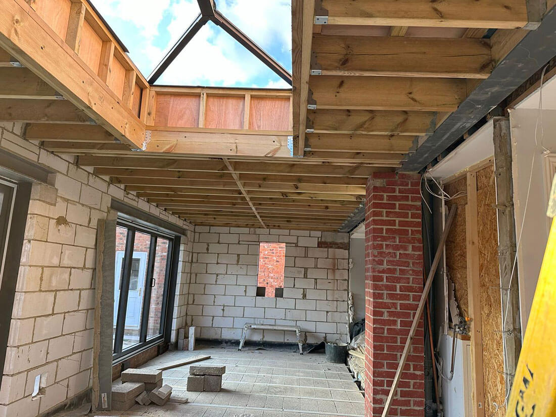 The inside of a new room shell, blockwork walls up, roof joists and a lantern opening overhead and a new opening formed through to the house